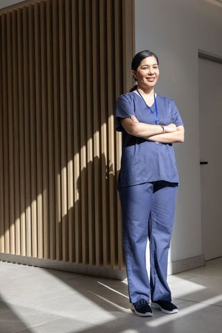 Confident female nurse in navy scrubs standing in sunlit clinic corridor with wood panels