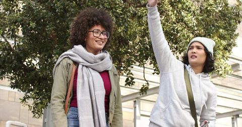 Friends hailing ride in urban plaza wearing scarves and hoodies, casual city lifestyle