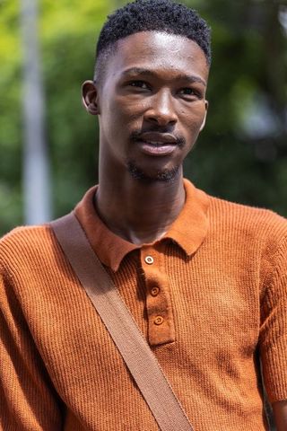 Young man wearing rust-orange knit polo carrying shoulder bag, looking right