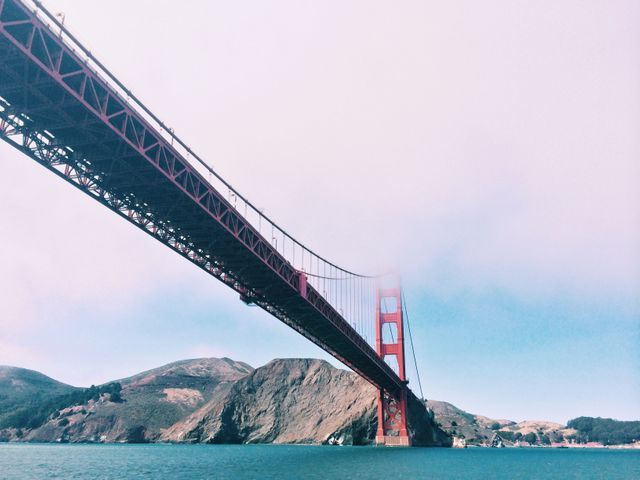 The Golden Gate Bridge is shown extending over the water with mountains in the background. This image emphasizes the iconic architecture of the bridge and the natural beauty of California. Perfect for use in travel and tourism promotions, architectural showcases, and California-themed marketing materials.