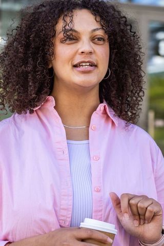 Urban woman talking while holding coffee cup in pink shirt, candid city portrait
