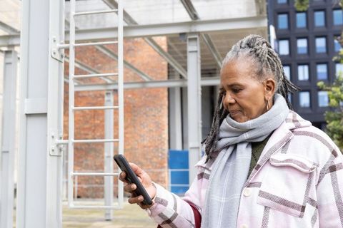 Senior woman checking smartphone in urban courtyard wearing plaid coat and gray scarf