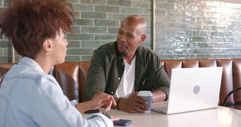 African american coworkers collaborating at cafe booth with laptop and takeaway coffee