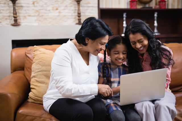 Happy multi-generation family using laptop together while sitting on sofa at home