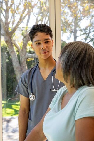 Male healthcare worker assisting senior woman by window