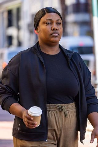 Confident african american woman walking downtown holding coffee and wearing red earbud