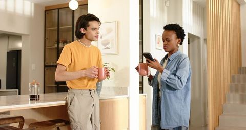 Multiracial couple sharing morning coffee and checking phone in open-plan minimalist kitchen