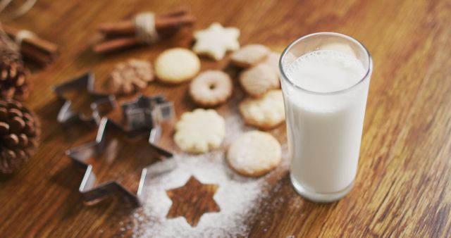 Cup of milk sitting on wooden table next to homemade cookies and baking tools creates a warm, festive atmosphere. Perfect for holiday-themed spreads, recipes, or lifestyle blogs focusing on baking and homely settings.