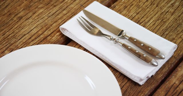 A dinner plate is set next to a fork and knife on a napkin, with copy space. The wooden table provides a warm background, suggesting a cozy dining atmosphere.