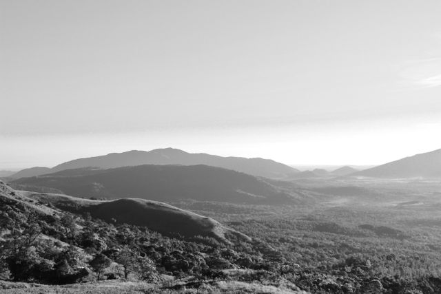 A tranquil black and white view showing a vast, scenic mountain range with lush valleys and hills in the foreground. This image captures the serenity and beauty of untouched wilderness and is perfect for backgrounds, nature-themed blogs, travel magazines, or any content aiming to inspire peace and reflection. Ideal for use in designs focused on simplicity, minimalism, and natural beauty.