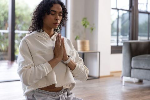 Non-binary adult meditating at home practicing mindfulness with smartwatch and rings