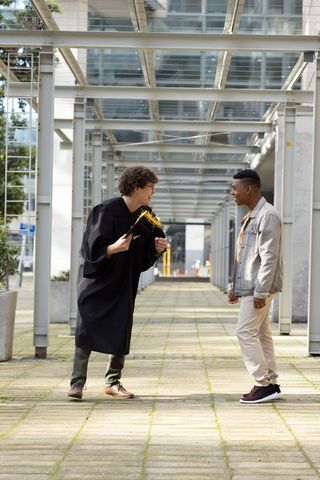 Friends celebrating graduate holding mortarboard with yellow tassel on campus walkway