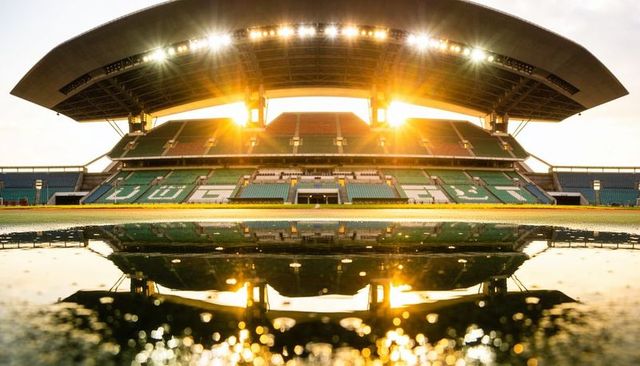 Sunset stadium grandstand glowing and reflecting in puddle under curved cantilevered roof