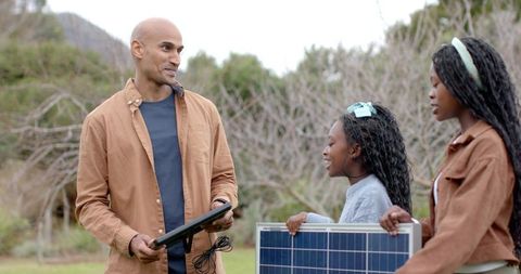 Father teaching daughters solar energy with meter while holding solar panel outdoors