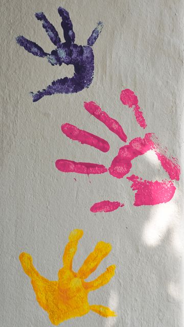 Three colorful handprints in purple, pink, and yellow are painted on a white wall, symbolizing creativity and playfulness. This can be used in educational settings, children's activities promotion, or art and crafts ideas. Perfect for illustrating themes of creativity, childhood, and artistic expression.