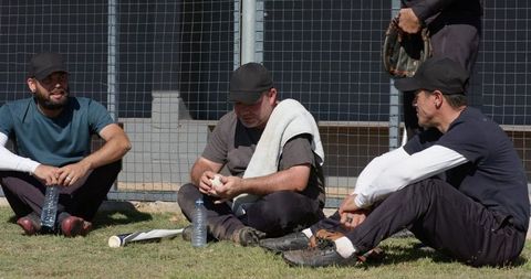 Baseball teammates resting on grass after practice sitting with gloves and water bottles