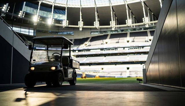 Utility golf cart emerging from tunnel casting silhouette against empty stadium bowl