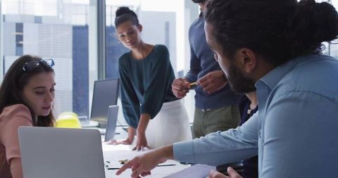 Design team collaborating over sketches and laptop with man pointing in modern city office