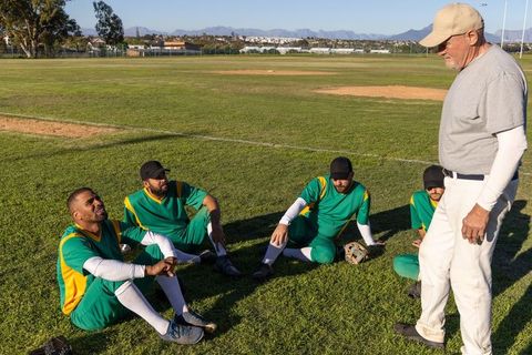 Baseball coach coaching players on field while team sitting listening during strategy talk