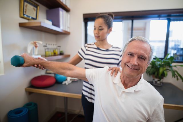 Senior man lifting dumbbell with assistance from female physiotherapist in hospital ward. Ideal for use in healthcare, elderly care, physical therapy, and rehabilitation contexts. Useful for illustrating patient care, fitness for seniors, and professional medical services.