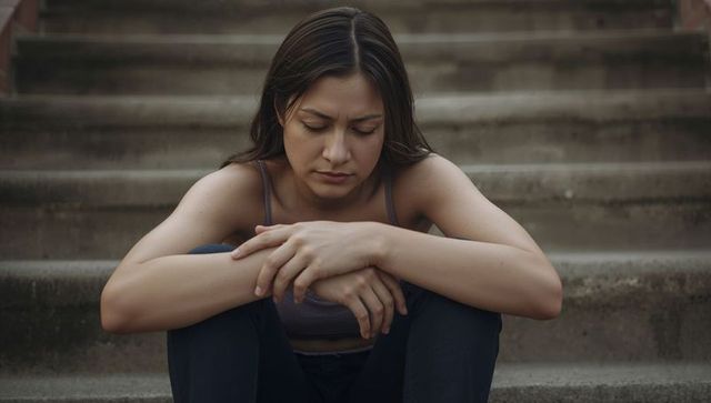 Young woman sitting on concrete stairs looking pensive and reflective, urban lifestyle