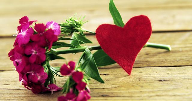 Red heart and vibrant pink flowers on rustic wooden table, symbolizing love and romance. Perfect for use in Valentine's Day promotions, romantic greeting cards, wedding themes, and anniversary celebrations.