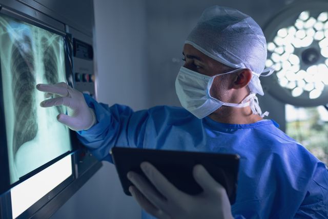 Surgeon in operating room examining x-ray on digital tablet, ideal for medical, healthcare, and technology-related content. Useful for illustrating surgical procedures, medical diagnostics, and hospital environments.