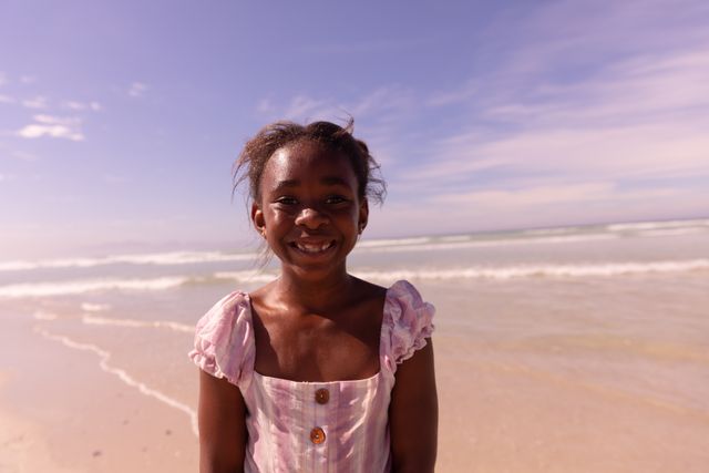 Portrait of smiling african american girl standing against sea and blue sky on sunny day, copy space. childhood, nature, unaltered, lifestyle, enjoyment and holiday concept.