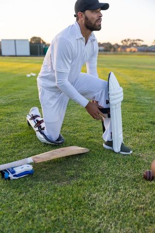 Cricketer adjusting leg pad on outfield during golden hour practice session