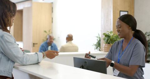 African american receptionist processing card payment at medical clinic reception desk