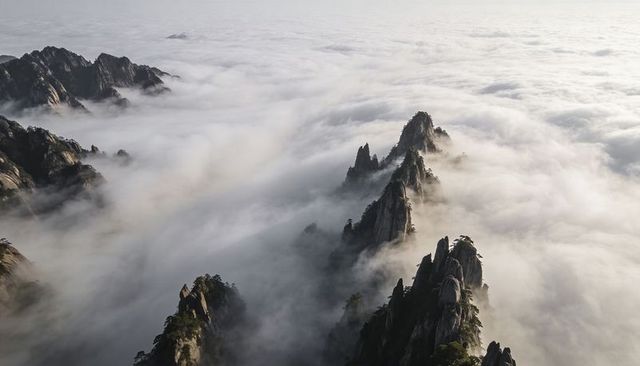 Jagged granite spires piercing sea of clouds over misty mountain ridges
