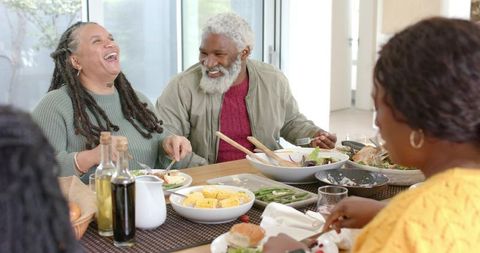 Multi-generational Black family laughing and sharing home-cooked meal around sunny dining table