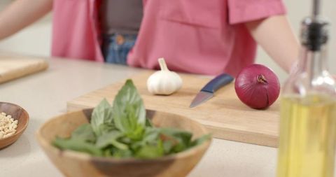 Asian man chopping garlic and red onion on cutting board with basil and olive oil prep