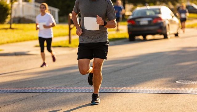 Runner crossing timing strip on sunny neighborhood road during community 5k race