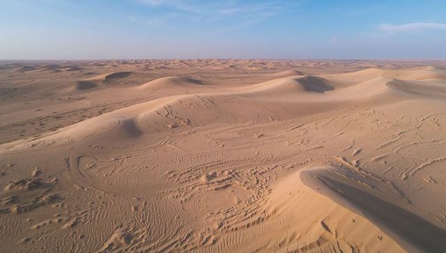 Shifting sand dunes stretching across vast desert, wind-sculpted ripples and tire tracks