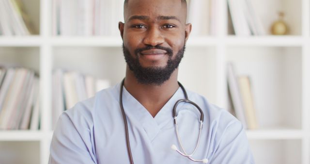 Young male doctor with stethoscope around neck, smiling confidently in medical office setting. Useful for healthcare advertisements, medical websites, brochures for clinics, hospital promotional materials, and public health campaigns.
