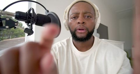 African man recording podcast pointing at camera wearing headphones and beanie