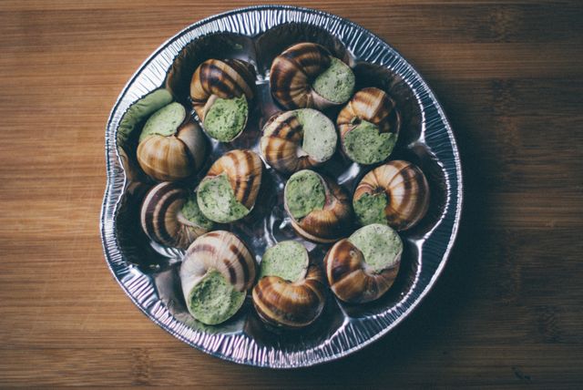 Gourmet escargot prepared with herb butter on aluminum baking tray, exquisite French cuisine as appetizer or gourmet meal, ideal for blog posts, food magazines, cooking websites, recipe illustrations.
