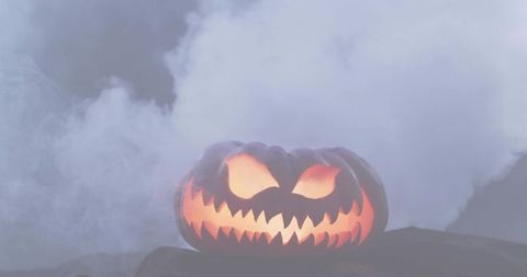 Glowing carved jack-o'-lantern casting eerie orange glow in swirling smoke