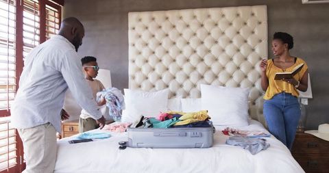 African American family packing luggage on bed while planning trip with notebook