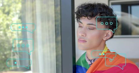 Contemplative man wearing rainbow flag and bandana leaning on window with chat bubbles