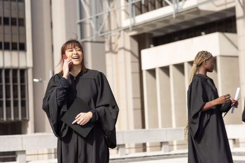 Asian and african-american graduates celebrating on campus terrace holding cap and diploma