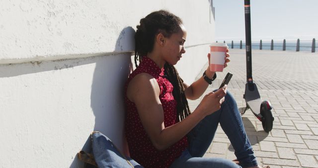 Woman Sitting Outdoors Drinking Coffee Using Mobile Phone Near Electric Scooter - Download Free Stock Images Pikwizard.com