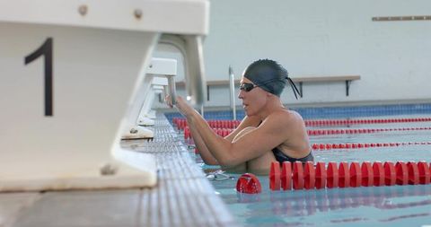 Mature swimmer resting at pool edge wearing swim cap and goggles beside lane 1