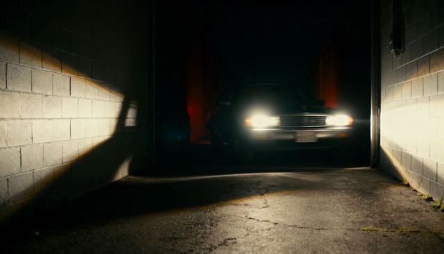 Sedan headlights piercing dark garage bay, casting dramatic wall shadows at night