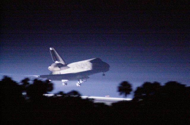 This captivating image shows the Space Shuttle Atlantis approaching touchdown on Runway 15 at Kennedy Space Center during the night. The shuttle is well lit by landing lights, highlighting its reentry after the STS-101 mission to the International Space Station. This image can be ideal for content related to space exploration, NASA missions, aerospace technology, and significant historical events in spaceflight.