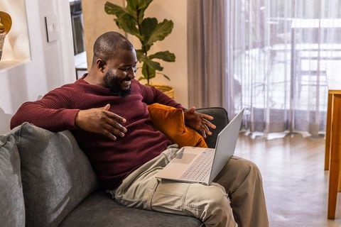 African american man having laptop video call while relaxing on cozy living room couch