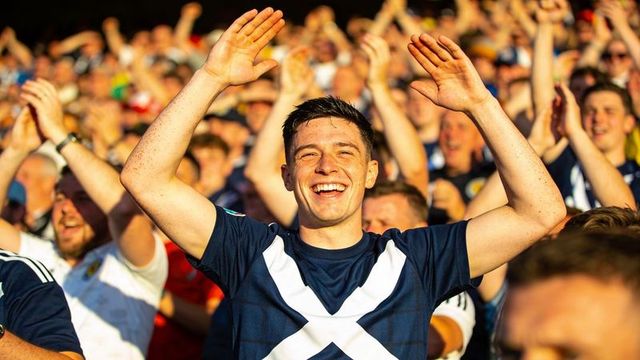 Cheering scottish football fan wearing navy jersey with white saltire raising hands