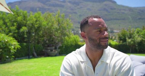 African american man relaxing on outdoor lounge in sunny backyard with mountain views