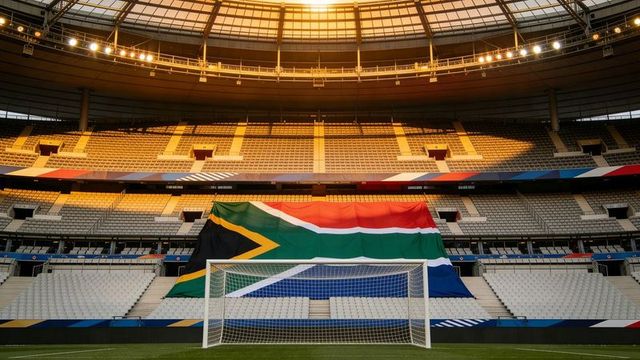 Giant south african flag draping over empty stadium seats, football goal at golden hour